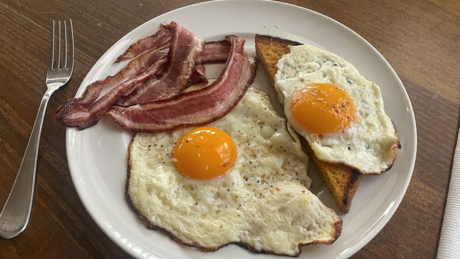 A breakfast plate of two fried eggs, crisp bacon and a slice of buttered toast