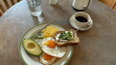 A plate of scrambled eggs, avocado and toast with a cup of black coffee