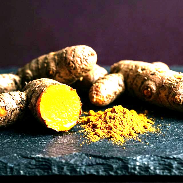 Fresh turmeric root and ground turmeric powder on a dark board