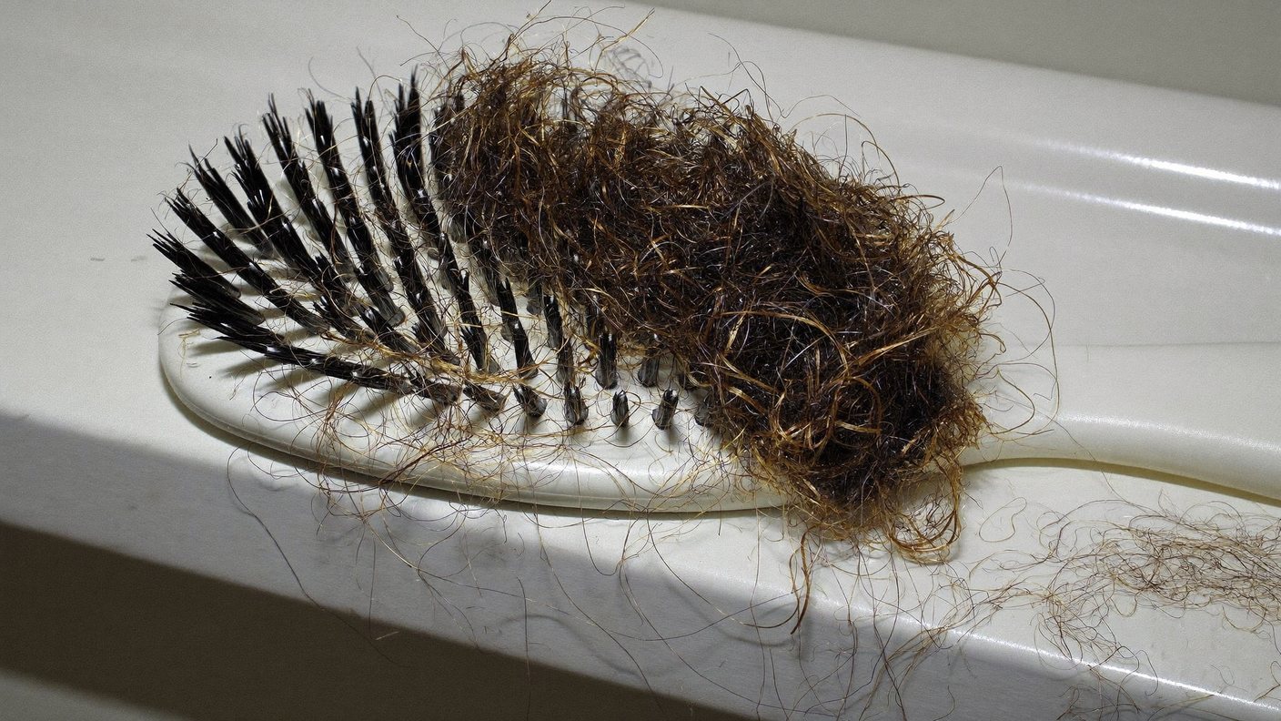 A hairbrush clogged with shed hair on a bathroom counter