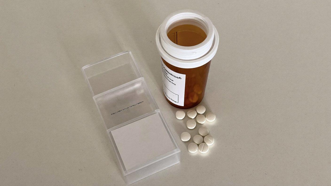 A prescription pill bottle and a weekly pill organiser on a counter